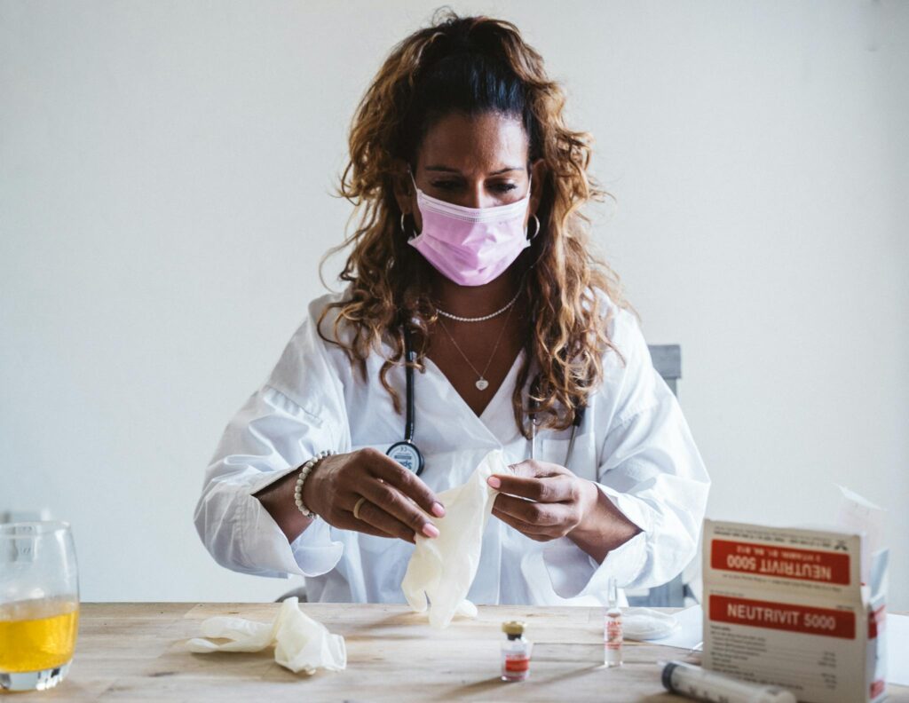 A female healthcare professional in a mask preparing medical supplies on a table indoors.